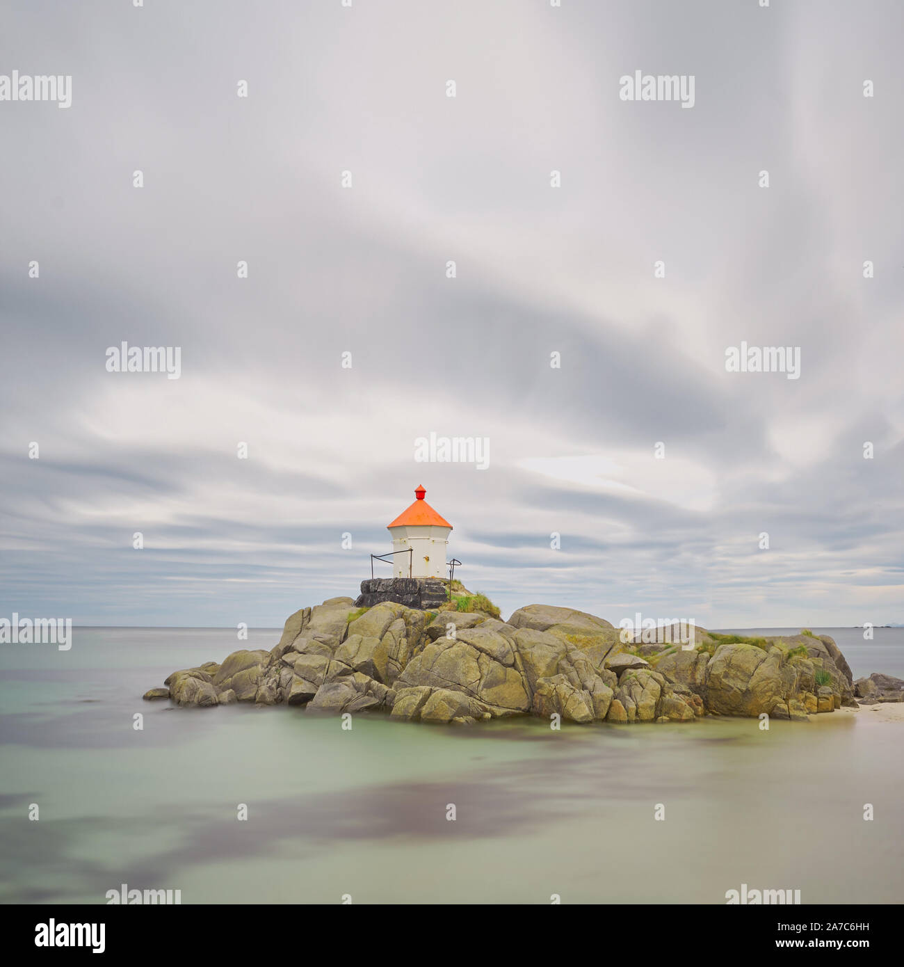 A small lighthouse stands on a rocky island in the middle of the sea ...