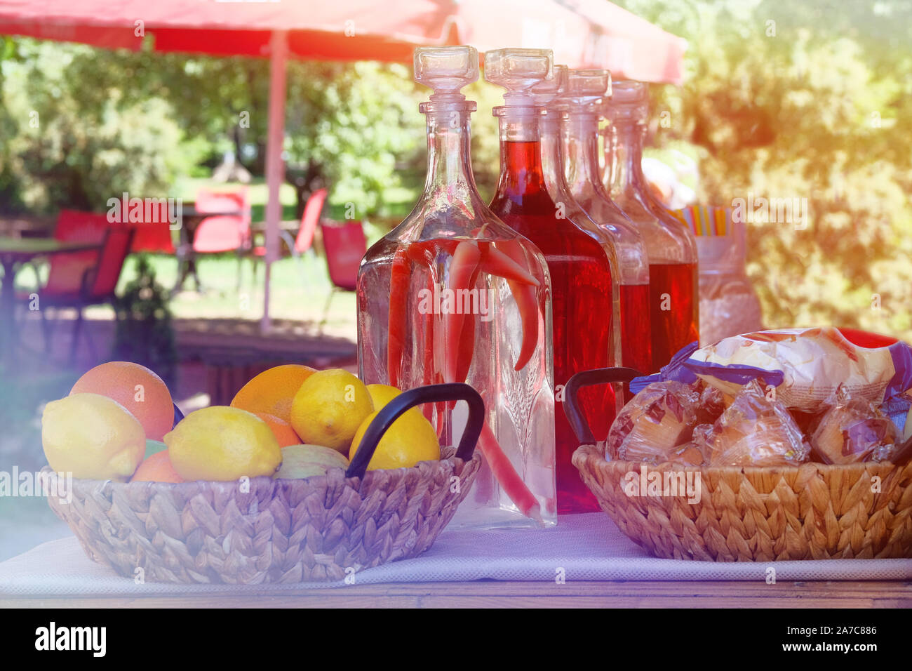 Traditional homemade infused vodka in vintage bottles with fruit and snacks in outdoor cafe. Alcohol drink with red pepper. Summer background and sunl Stock Photo