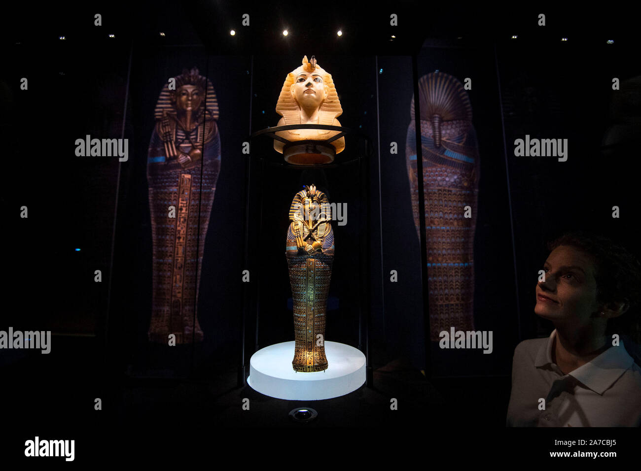 A staff members looks at a calcite stopper for a canopic jar of the King's Head, and a gold inlaid canopic coffinette of Tutankhamum, dated 1336-1326 BC, at a press preview for the Tutankhamun: Treasures of the Golden Phaorah exhibition at the Saatchi Gallery in Chelsea, London. PA Photo. Picture date: Friday November 1,2019. See PA story ARTS Tutankhamun . Photo credit should read: Victoria Jones/PA Wire Stock Photo