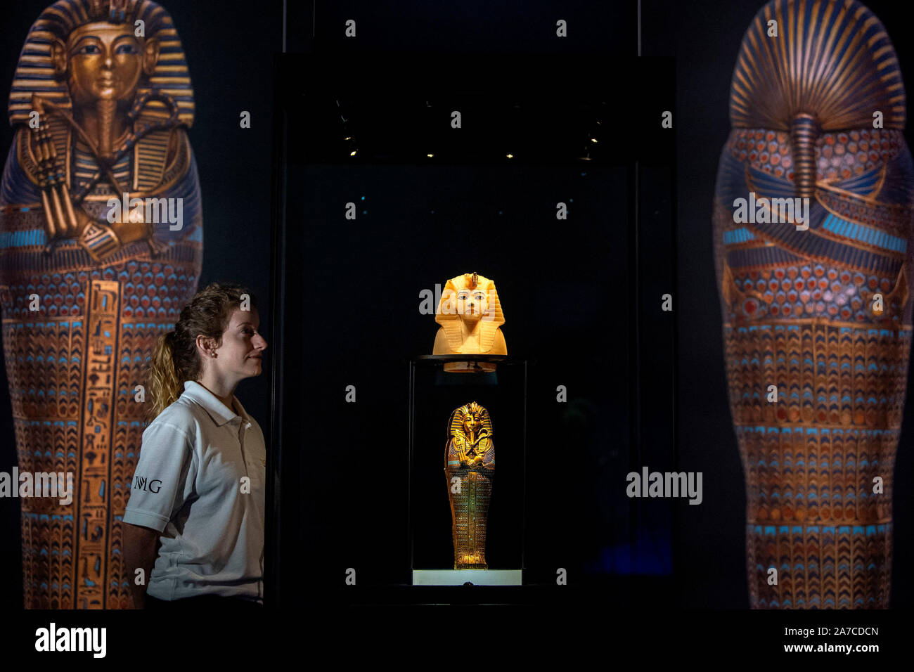 A staff member looks at a calcite stopper for a canopic jar of the King's Head, and a gold inlaid miniature canopic coffinette of Tutankhamum, dated 1336-1326 BC, at a press preview for the Tutankhamun: Treasures of the Golden Phaorah exhibition at the Saatchi Gallery in Chelsea, London. PA Photo. Picture date: Friday November 1,2019. See PA story ARTS Tutankhamun . Photo credit should read: Victoria Jones/PA Wire Stock Photo