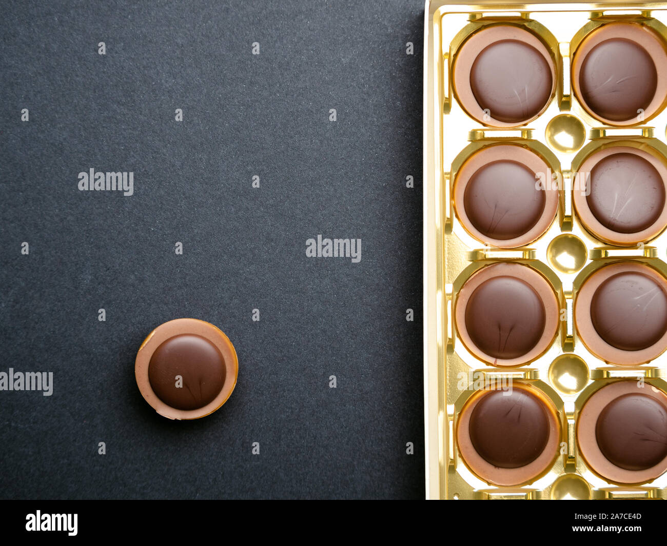Chocolate candies in a gold box over black background, top view Stock