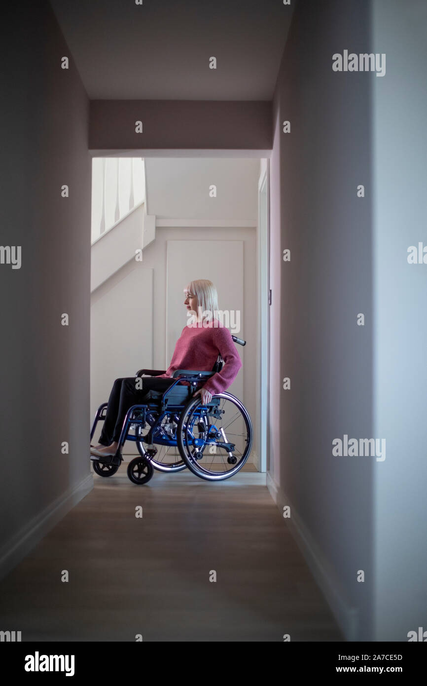 Woman Sitting In Wheelchair At Home In Hallway Stock Photo