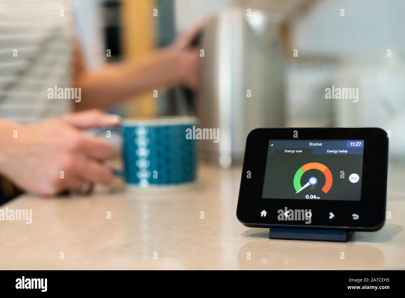 Woman At Home Boiling Kettle For Hot Drink With Smart Energy Meter In Foreground Stock Photo