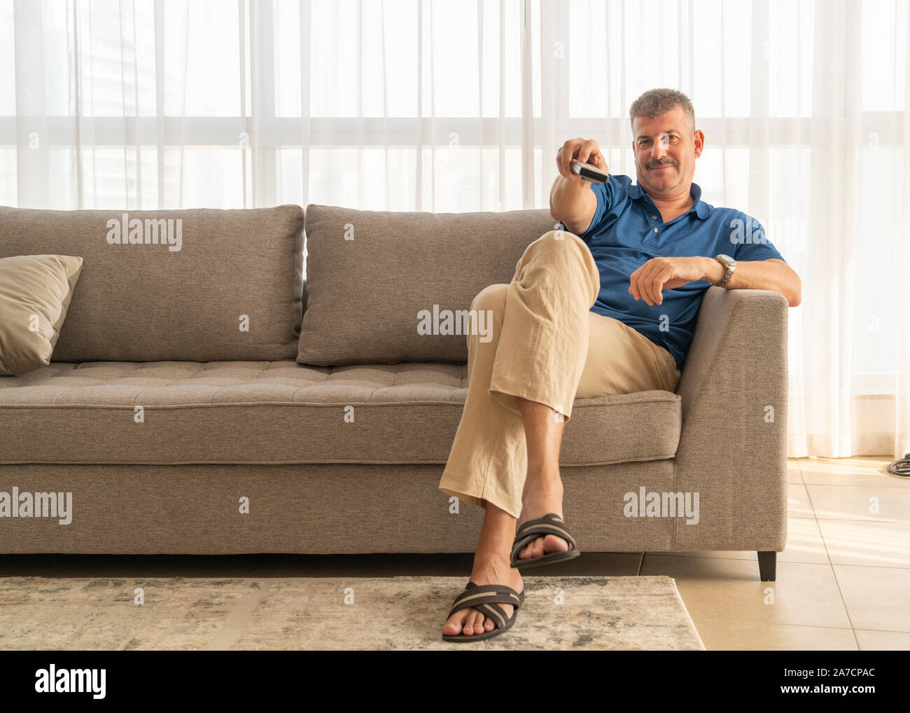 middle aged man sitting on a sofa and watching TV Stock Photo