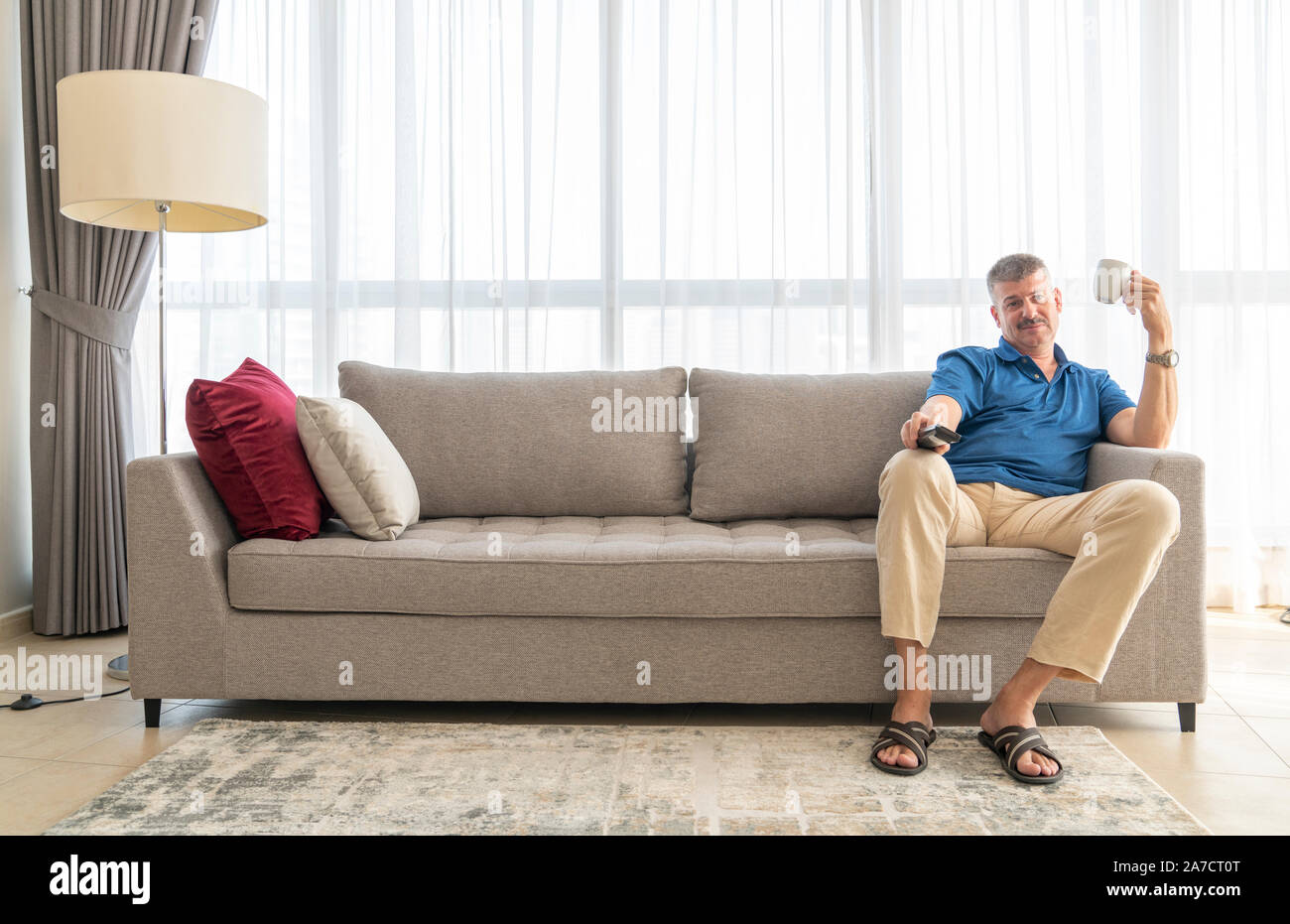 middle aged man sitting on a sofa and watching TV Stock Photo