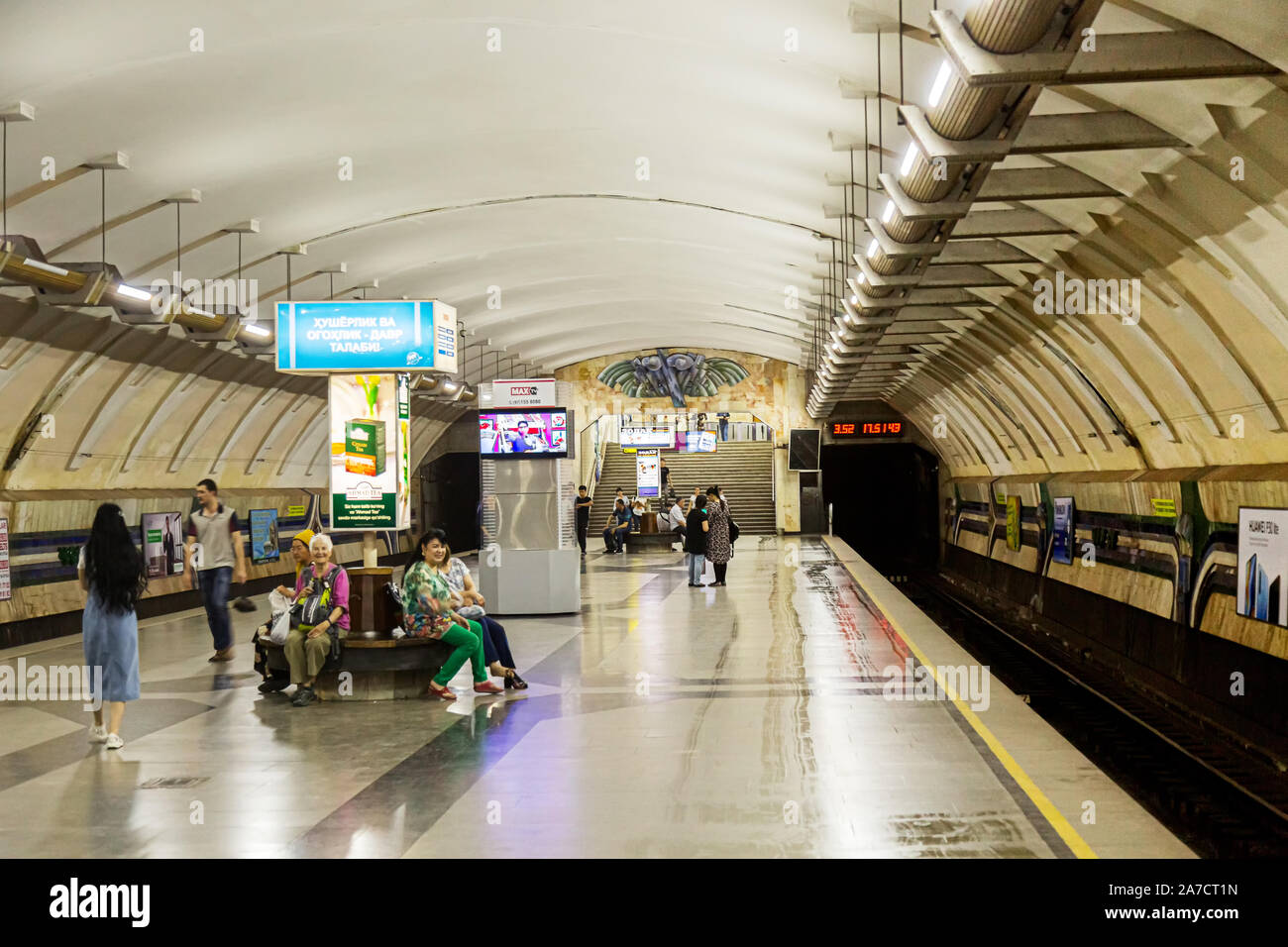 A number of passengers sit or stand around waiting for a train to arrive at Chorus Metro Tashkent. Stock Photo