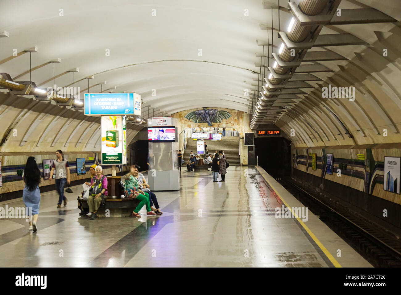 A number of passengers sit or stand around waiting for a train to arrive at Chorus Metro Tashkent. Stock Photo
