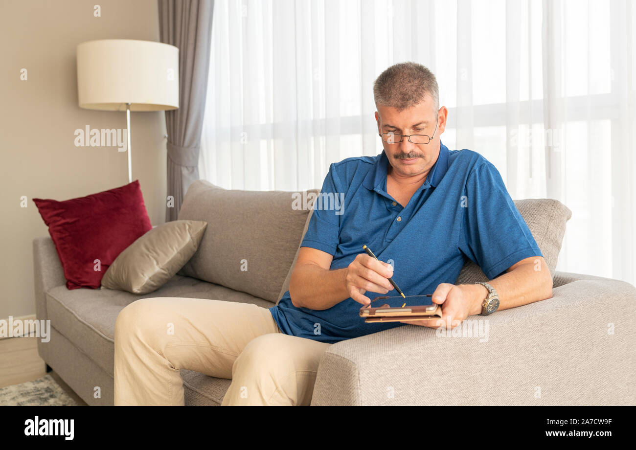 middle aged man working on his tablet on a sofa Stock Photo