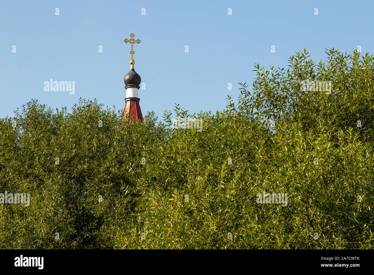Maroon top of orthodox church bell tower with cross against sky and trees Stock Photo