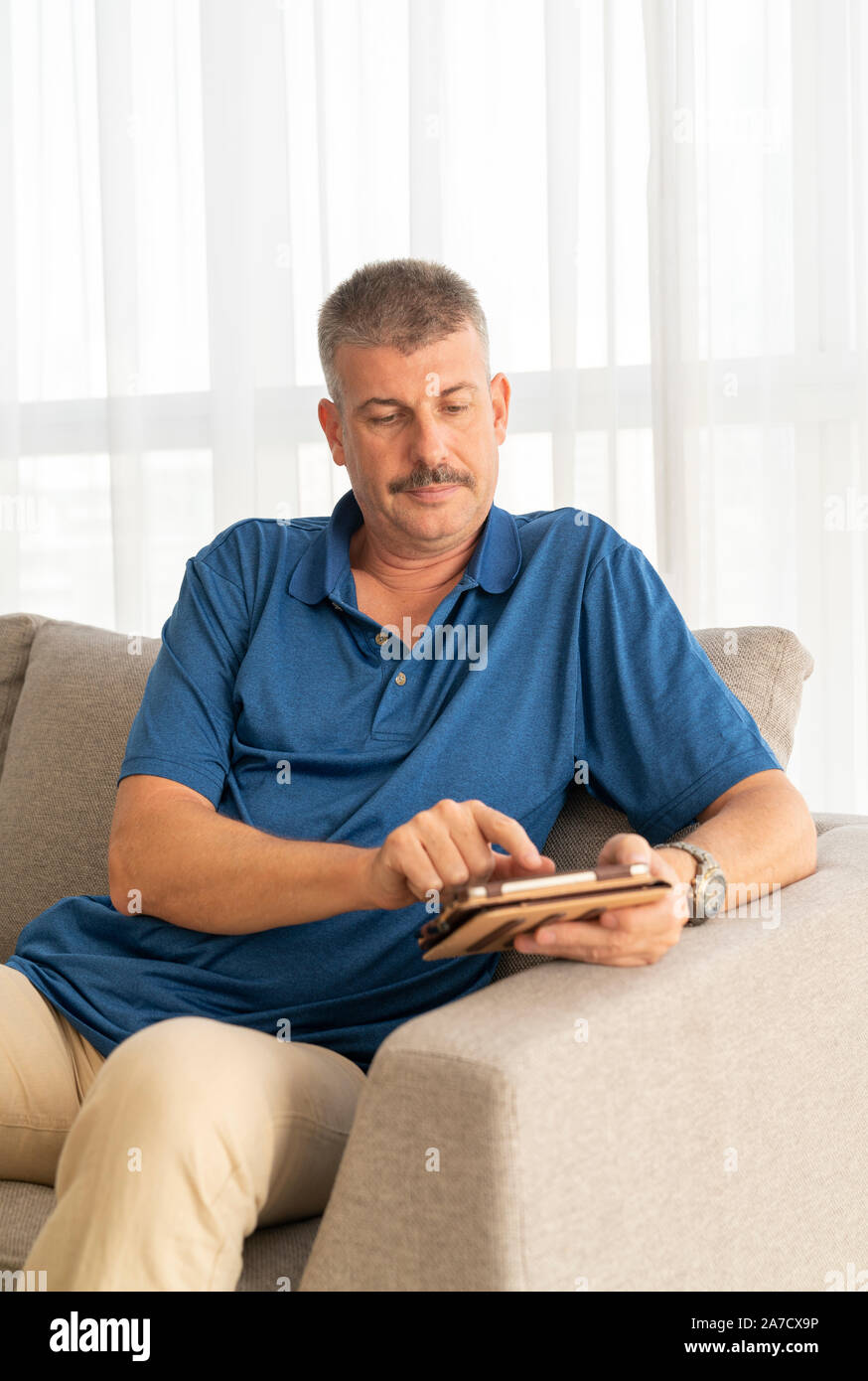 middle aged man working on his tablet on a sofa Stock Photo