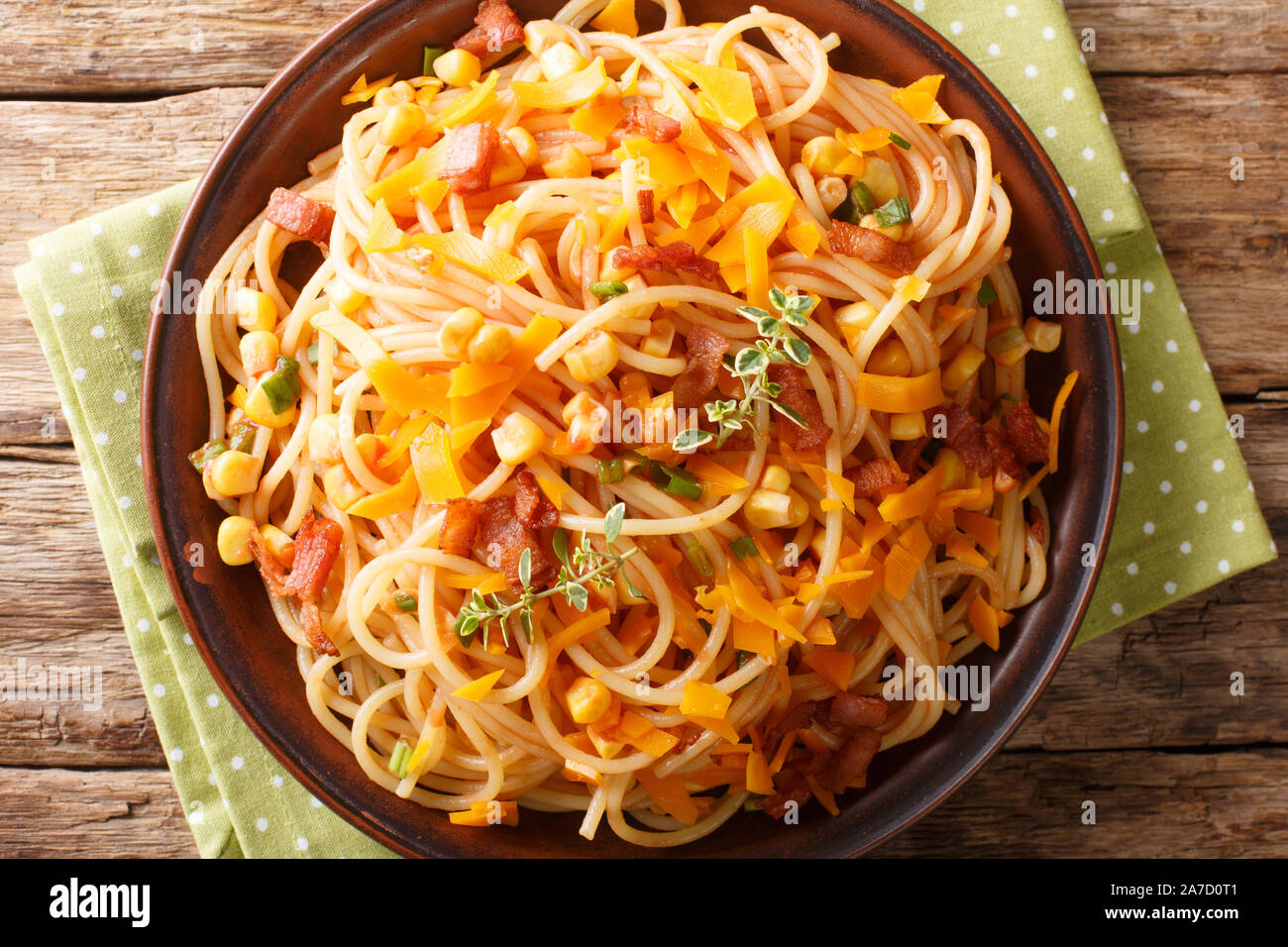 Spaghetti pasta salad with bacon, corn and Mimolette cheese close-up on a plate on the table. Horizontal top view from above Stock Photo