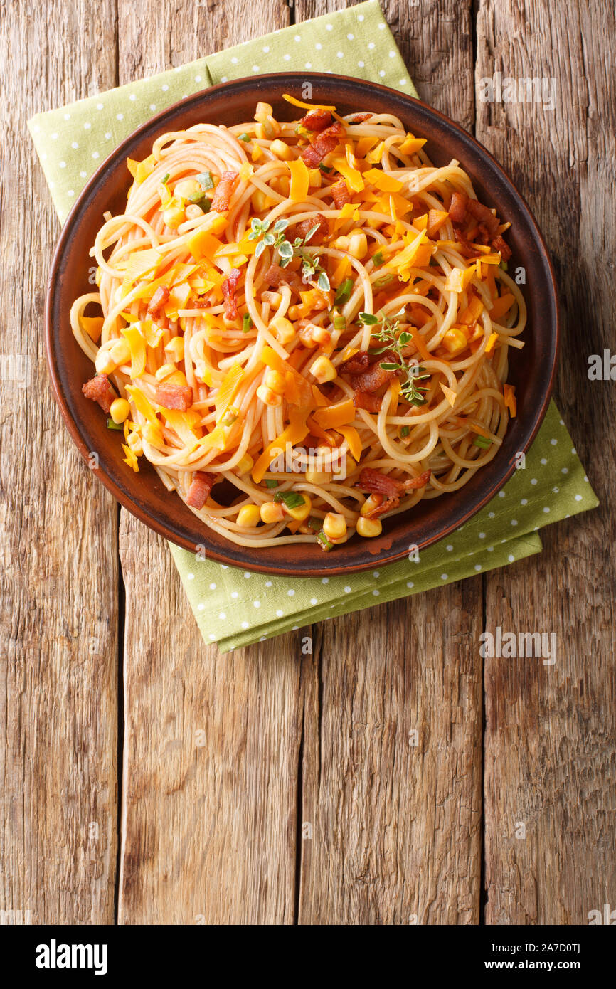Hot Italian spaghetti with bacon, corn and Mimolette cheese close-up on a plate on the table. Vertical top view from above Stock Photo