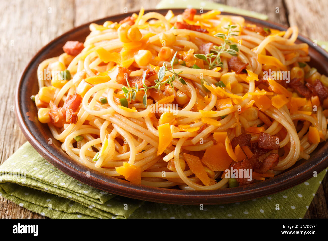 Spaghetti pasta salad with bacon, corn and Mimolette cheese close-up on a plate on the table. horizontal Stock Photo