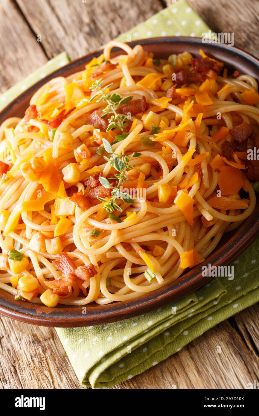Spaghetti with bacon, corn and cheese  Mimolette close-up on a plate on the table. vertical Stock Photo