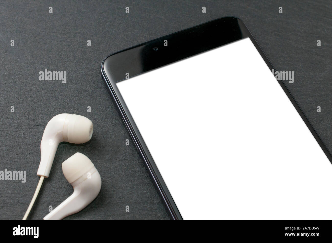 Blank screen smartphone on stone table with a set of white earphones Stock Photo