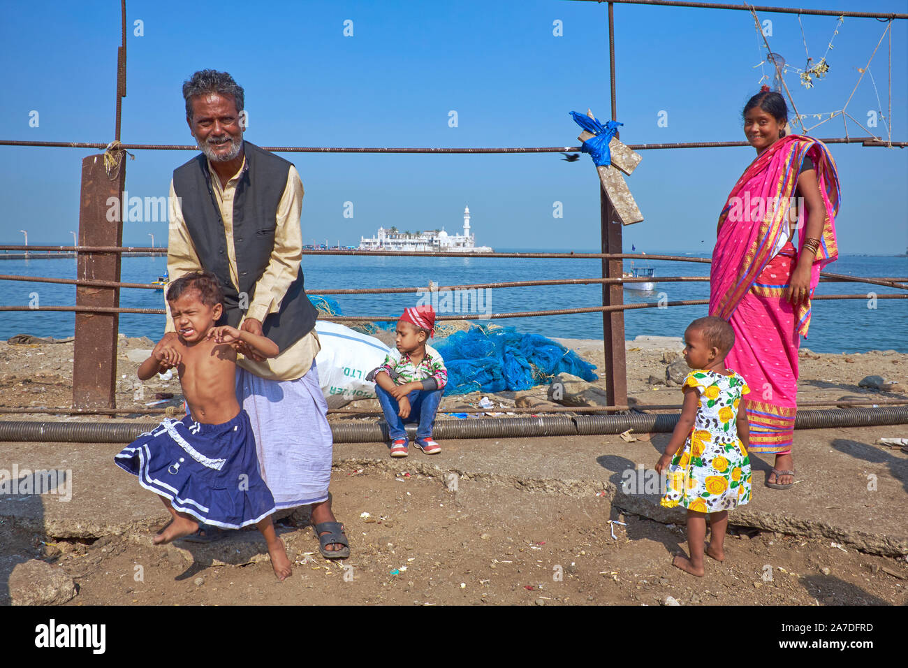 A sightseeing Muslim family of five at Worli Bay, Mumbai, India, the iconic Haji Ali Mosque in the b/g, the father trying to control his unruly son Stock Photo