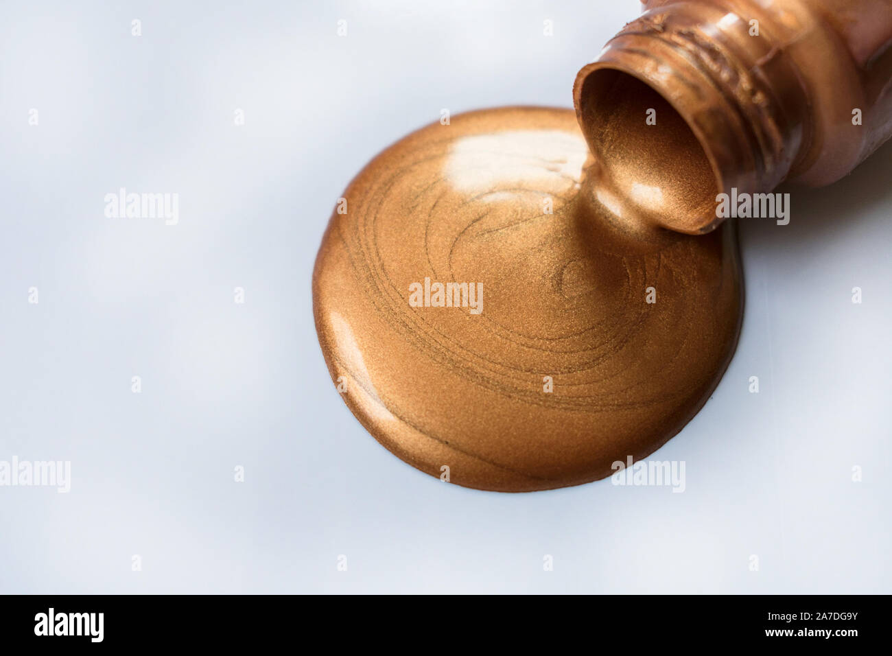 Copper-colored paint pouring from a bottle on a white background. Copy space. Stock Photo