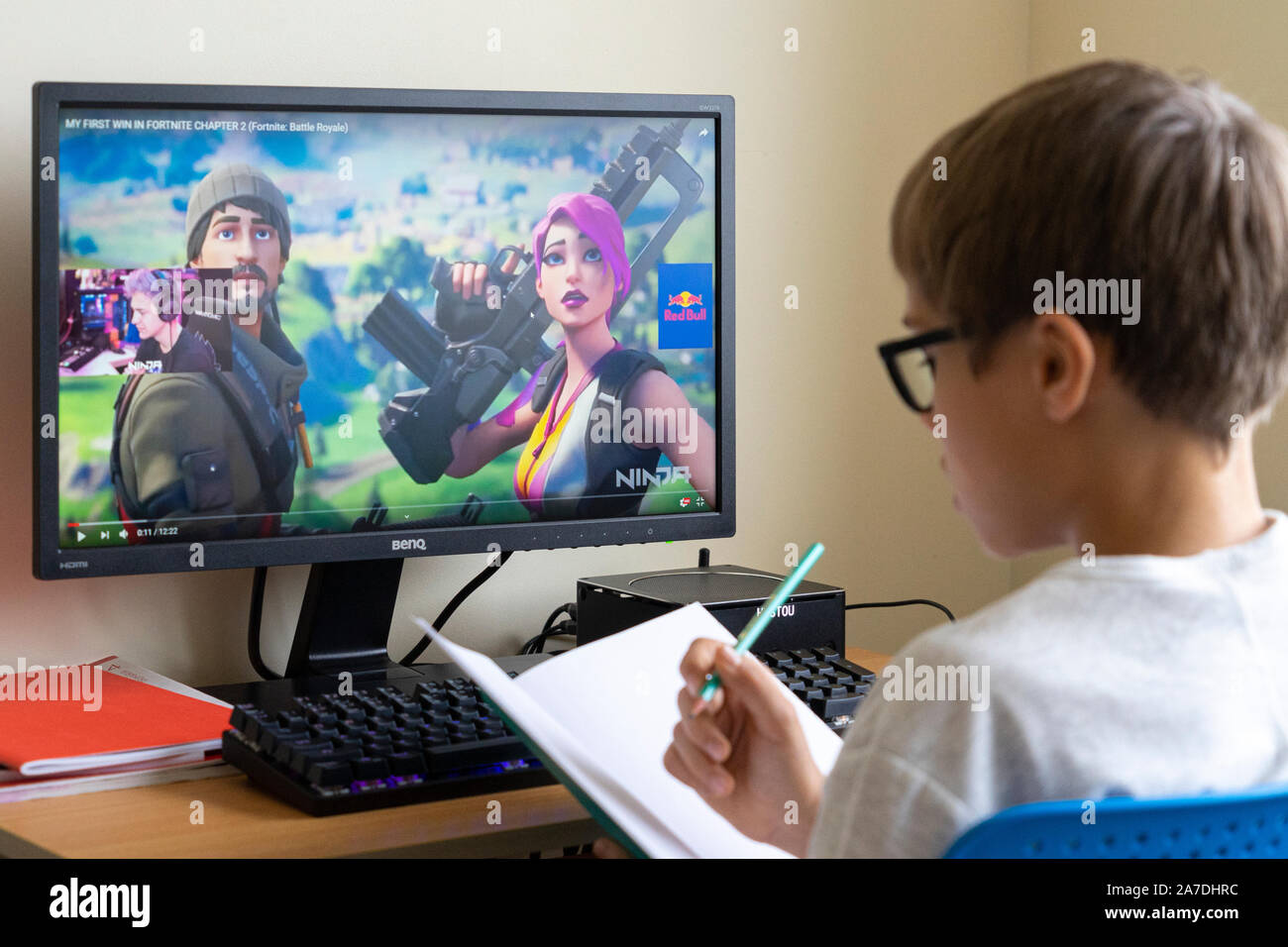 Boy doing homework and watching people play strategy video games and streaming on YouTube. Vilnius, Lithuania - 19 October 2019 Stock Photo