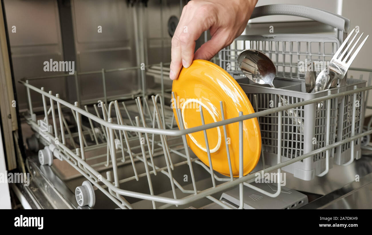 Man puts a dirty plates and cutlery in dishwasher. Top view, closeup
