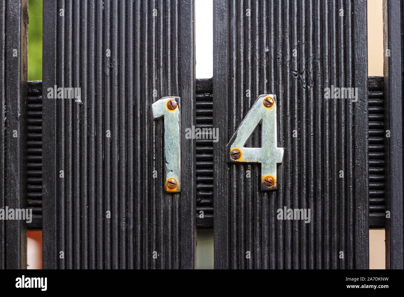 Rusty house number 14 on a black wooden gate with lines Stock Photo