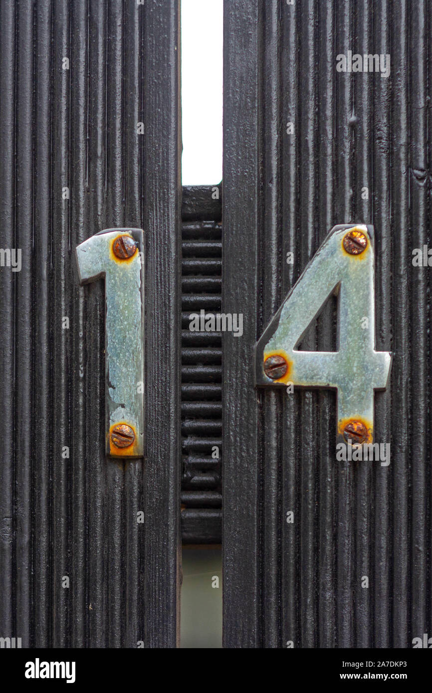 Rusty house number 14 on a black wooden gate with lines Stock Photo