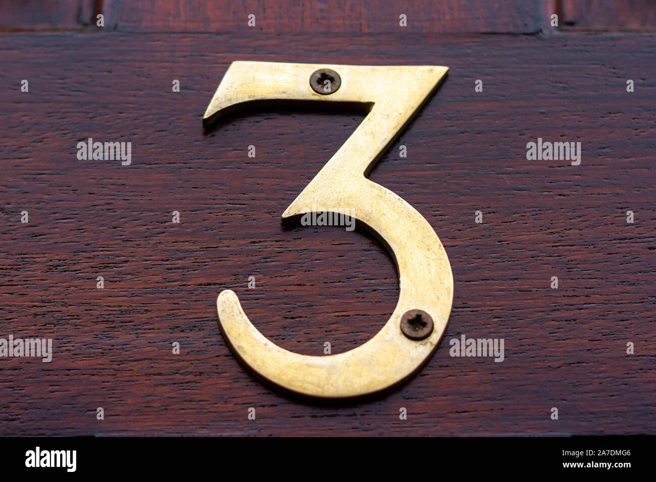 Large and elegant bronze house number 3 on a reddish wooden front door Stock Photo