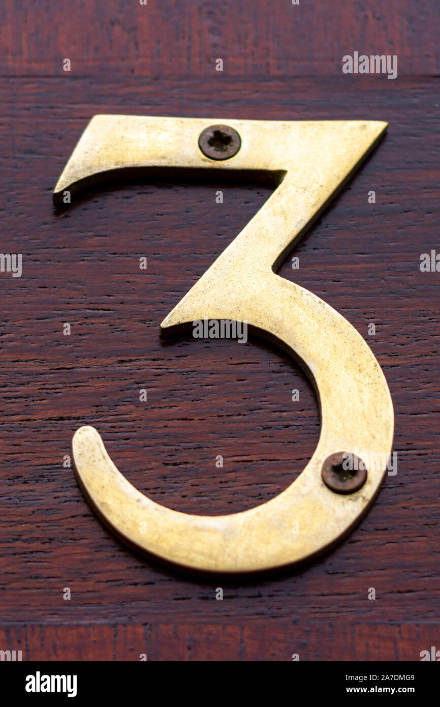 Large and elegant bronze house number 3 on a reddish wooden front door Stock Photo