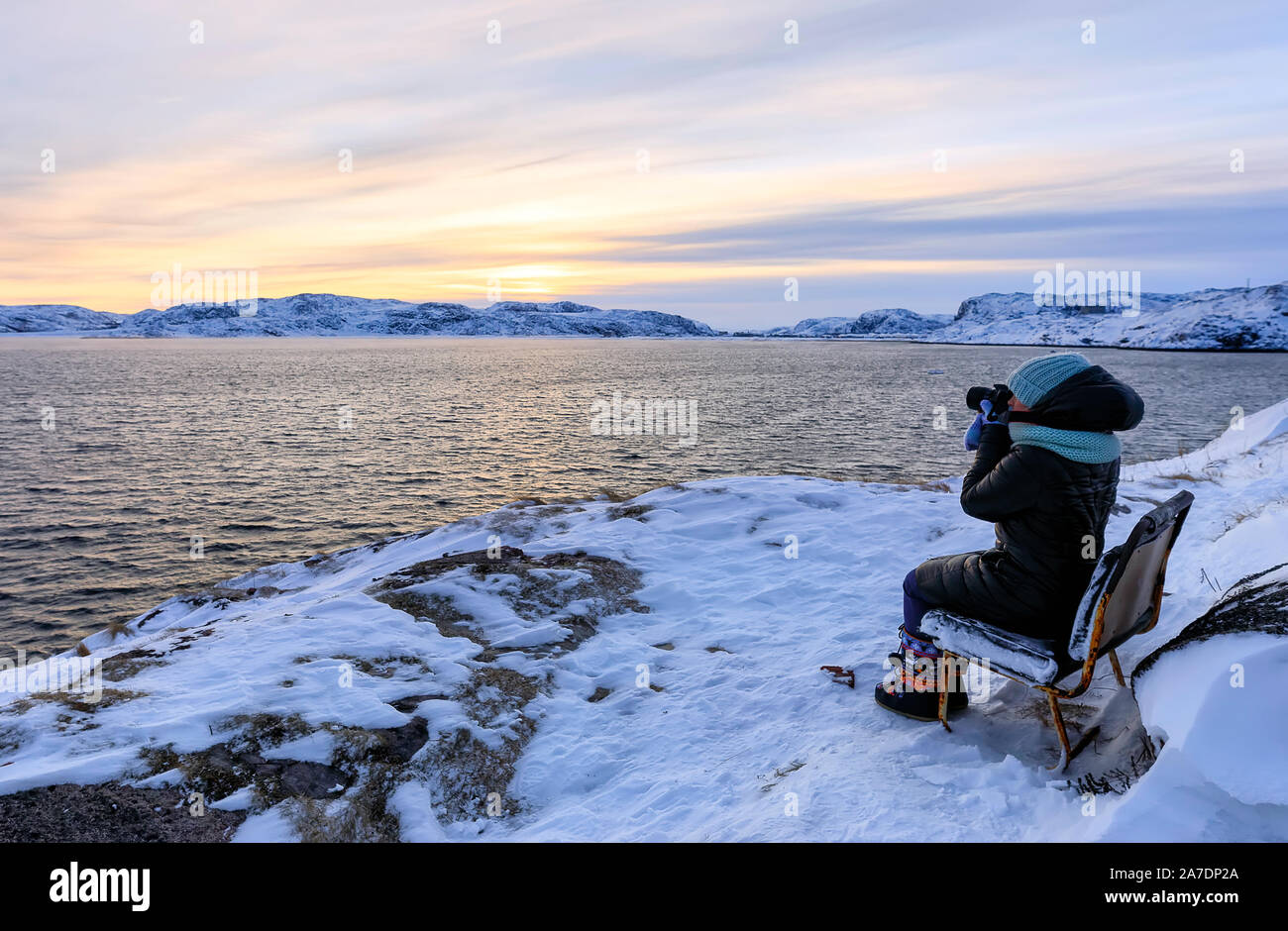 Young women traveler taking a photo on the beach of the Barents sea at sunset, Teriberka, Murmansk region, Russia. Adventure travel lifestyle concept Stock Photo