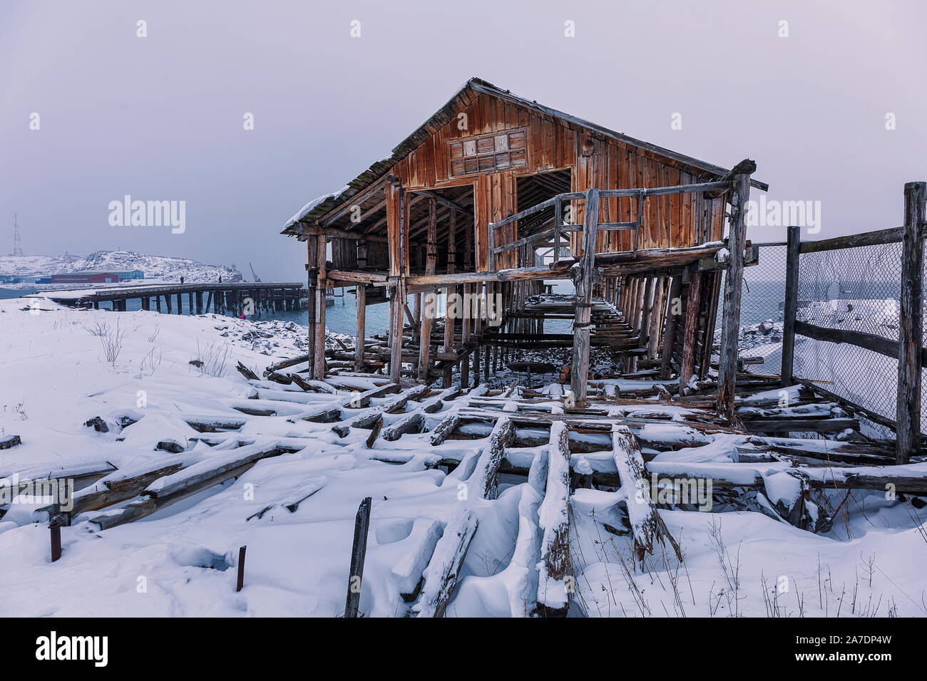 Old abandoned wooden factory against the background of a fish factory. Polar day.  Teriberka, Murmansk district. Kola Peninsula. Russian polar region. Stock Photo