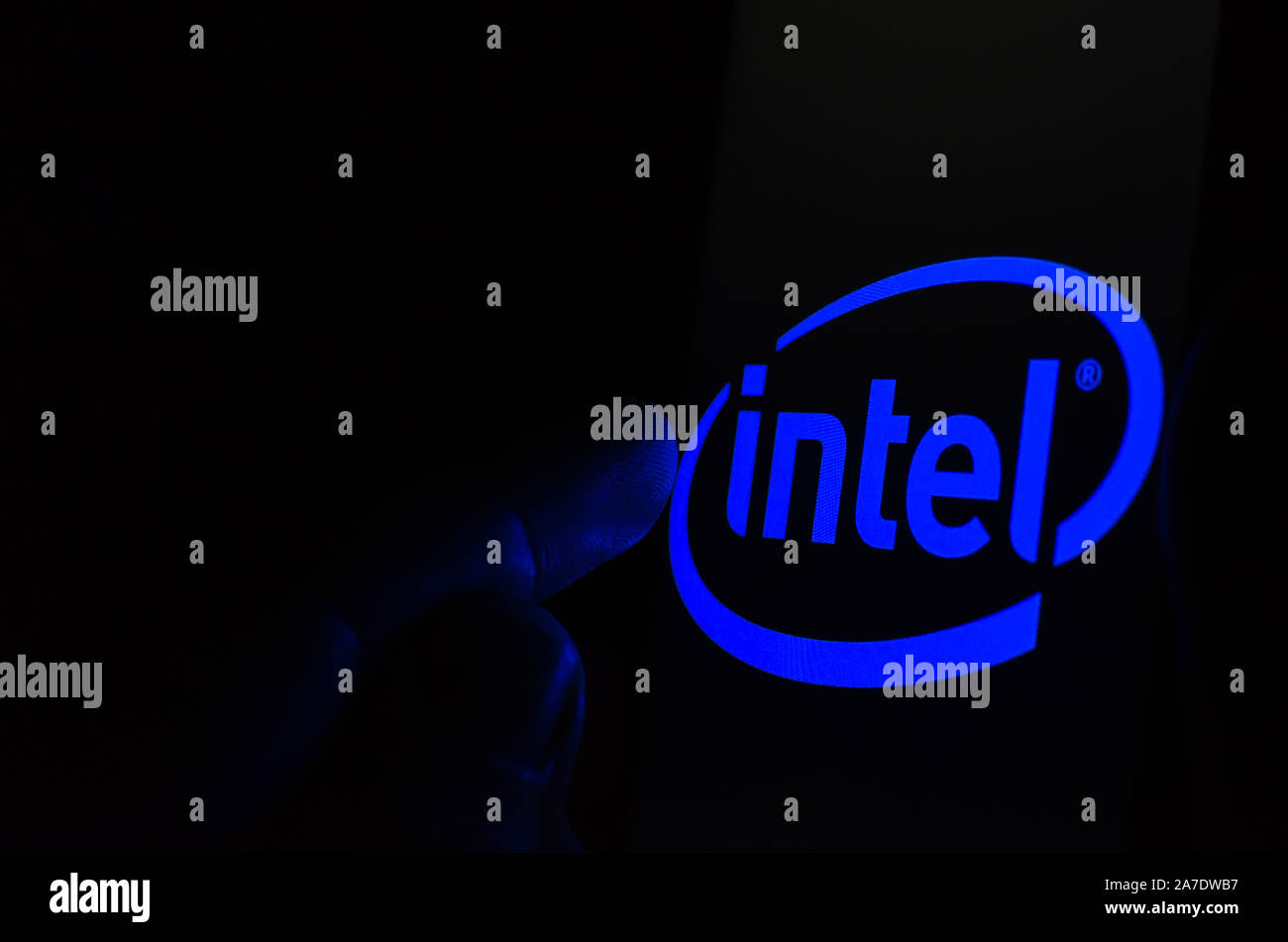 Intel logo on a smartphone screen in a dark room and a finger touching it. Stock Photo