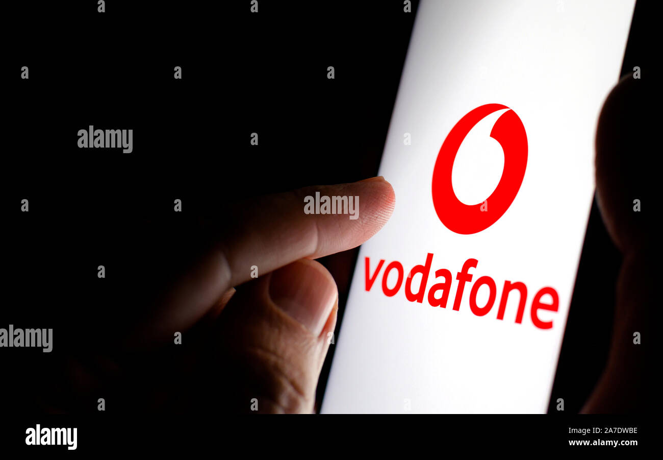 Vodafone logo on a smartphone screen in a dark room and a finger touching it. Stock Photo