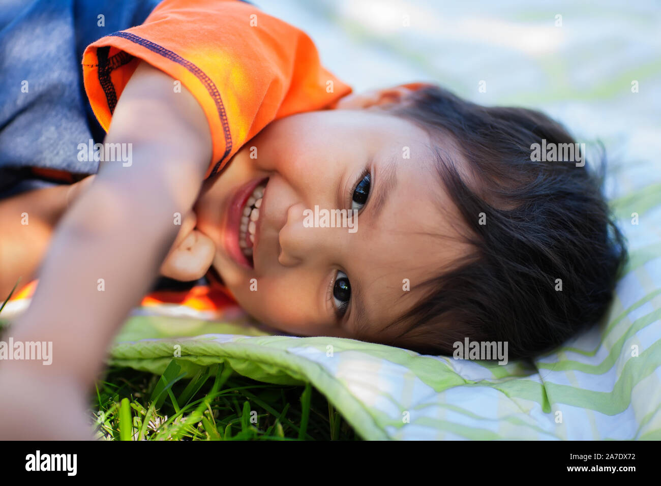 The cute smile of a young boy that is laying down on a picnic blanket, that awoke from a daytime nap. Stock Photo