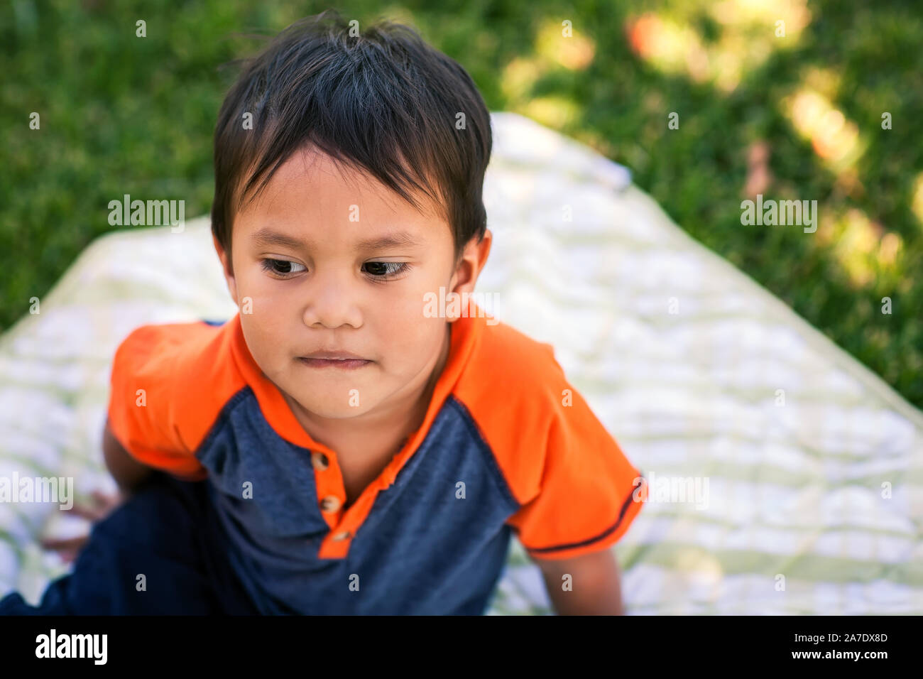 A little boy sitting in a picnic blanket looking sad and thoughtful. Stock Photo