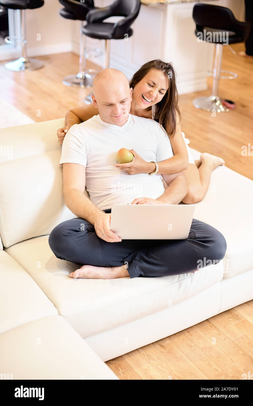 A young couple relaxing on the sofa with a laptop. Social networking. Concept of love, happiness, people and fun. Family concept, happy family. Stock Photo
