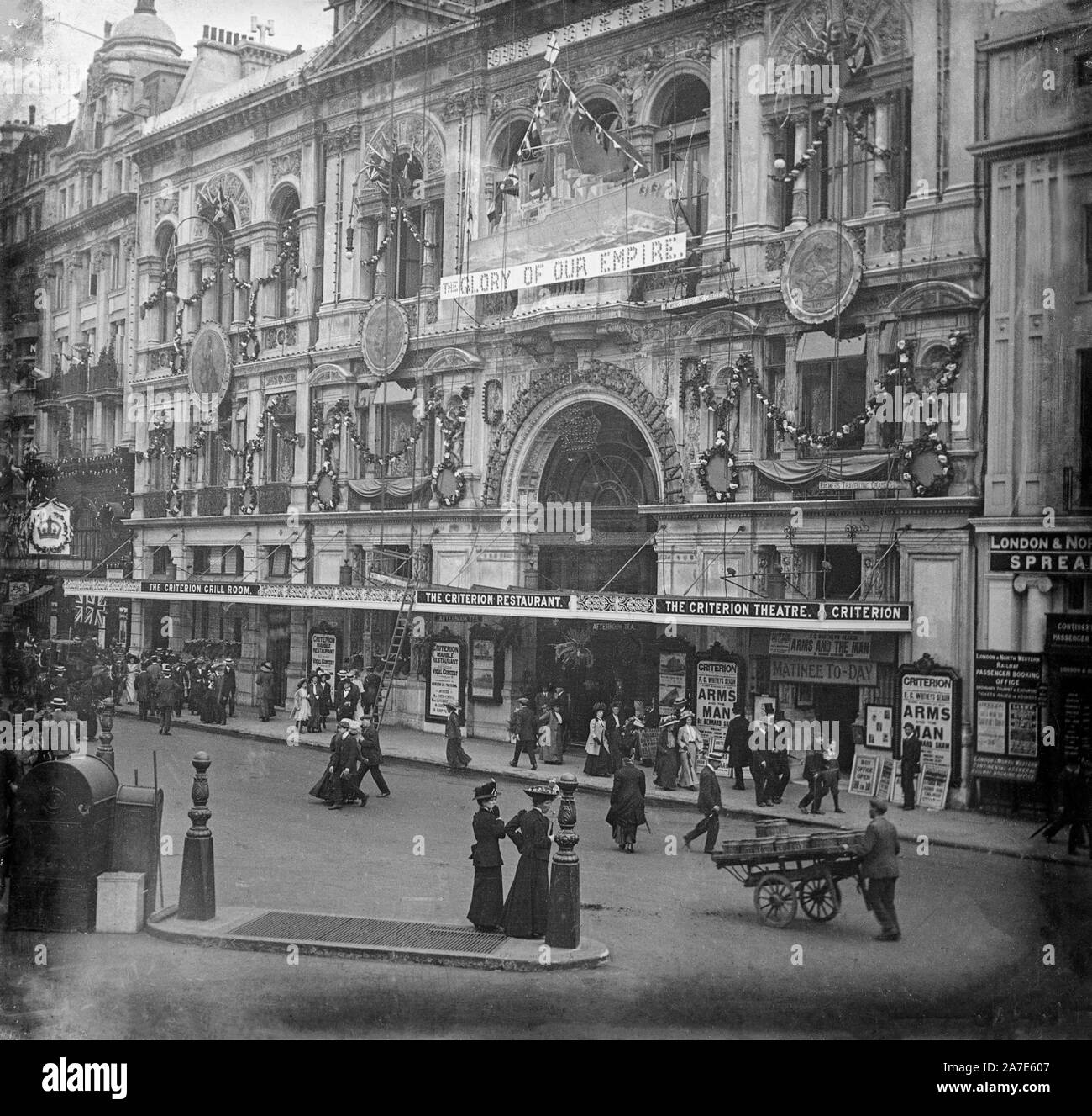 A vintage late Victorian black and white photograph showing the Criterion Theatre in Jermyn Street, London, England. The theatre is showing production of 'Arms and the Man' by Bernard Shaw. Many people are on the streets, showing typical fashion of the time. Stock Photo
