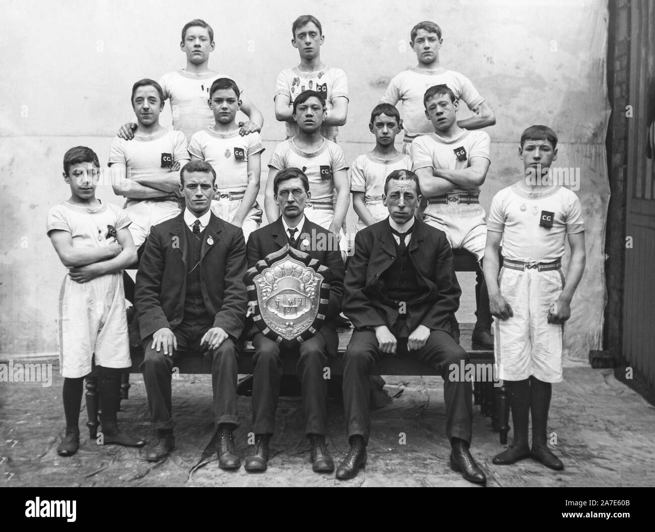 A vintage late Victorian early Edwardian black and white photograph showing a group of young English boy gymnasts posing for a camera whilst their coach or manager shows a large trophy shield. Stock Photo