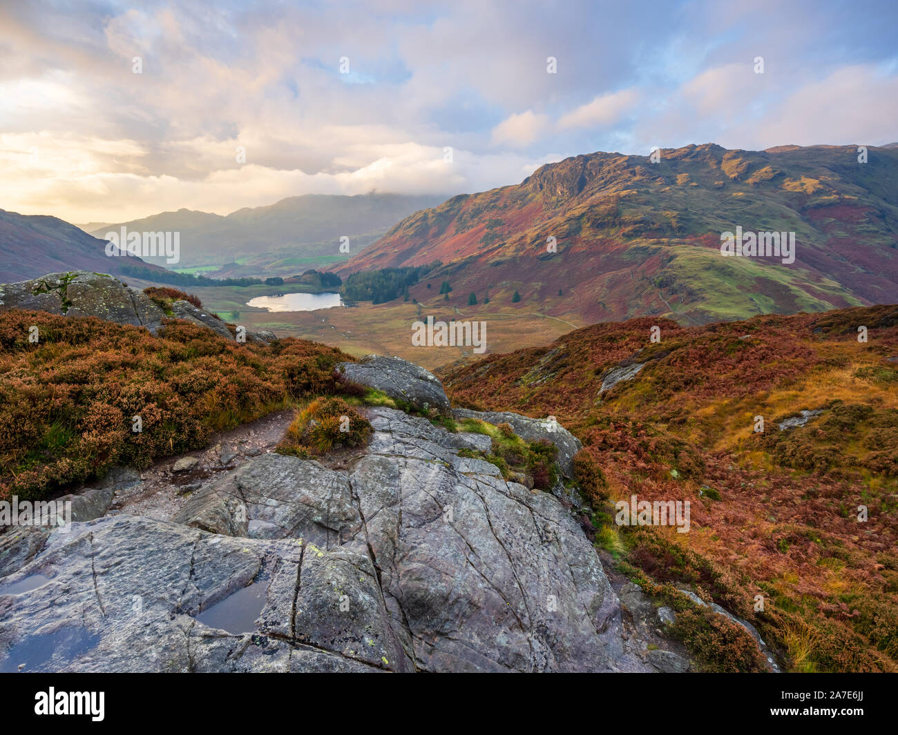 Blea Tarn is visible beneath the imposing slopes of Wrynose Fell during the golden hour of an autmn morning on Side Pike in The Lake District. Stock Photo