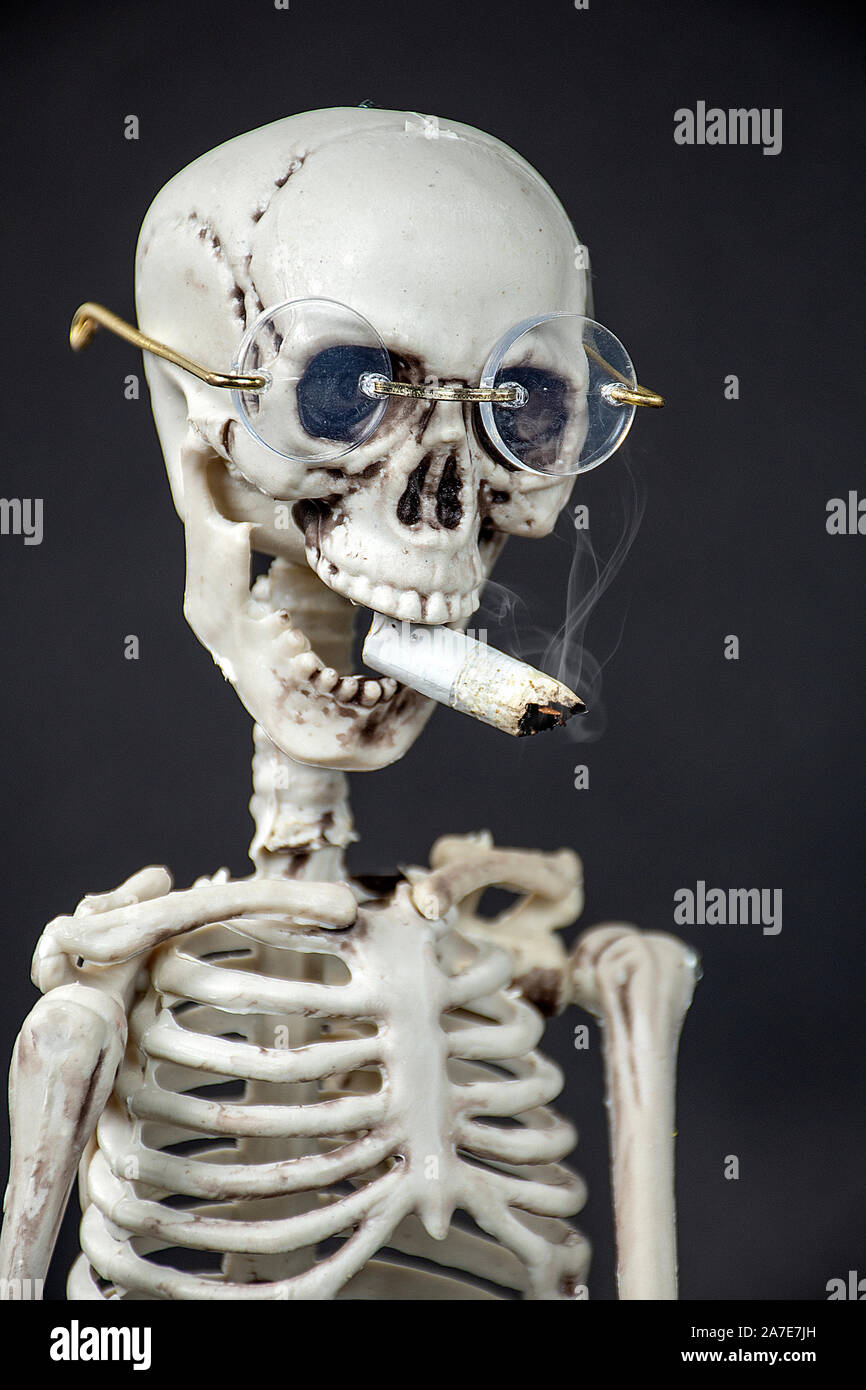 close up of skeleton wearing glasses smoking a cigarette on black background Stock Photo