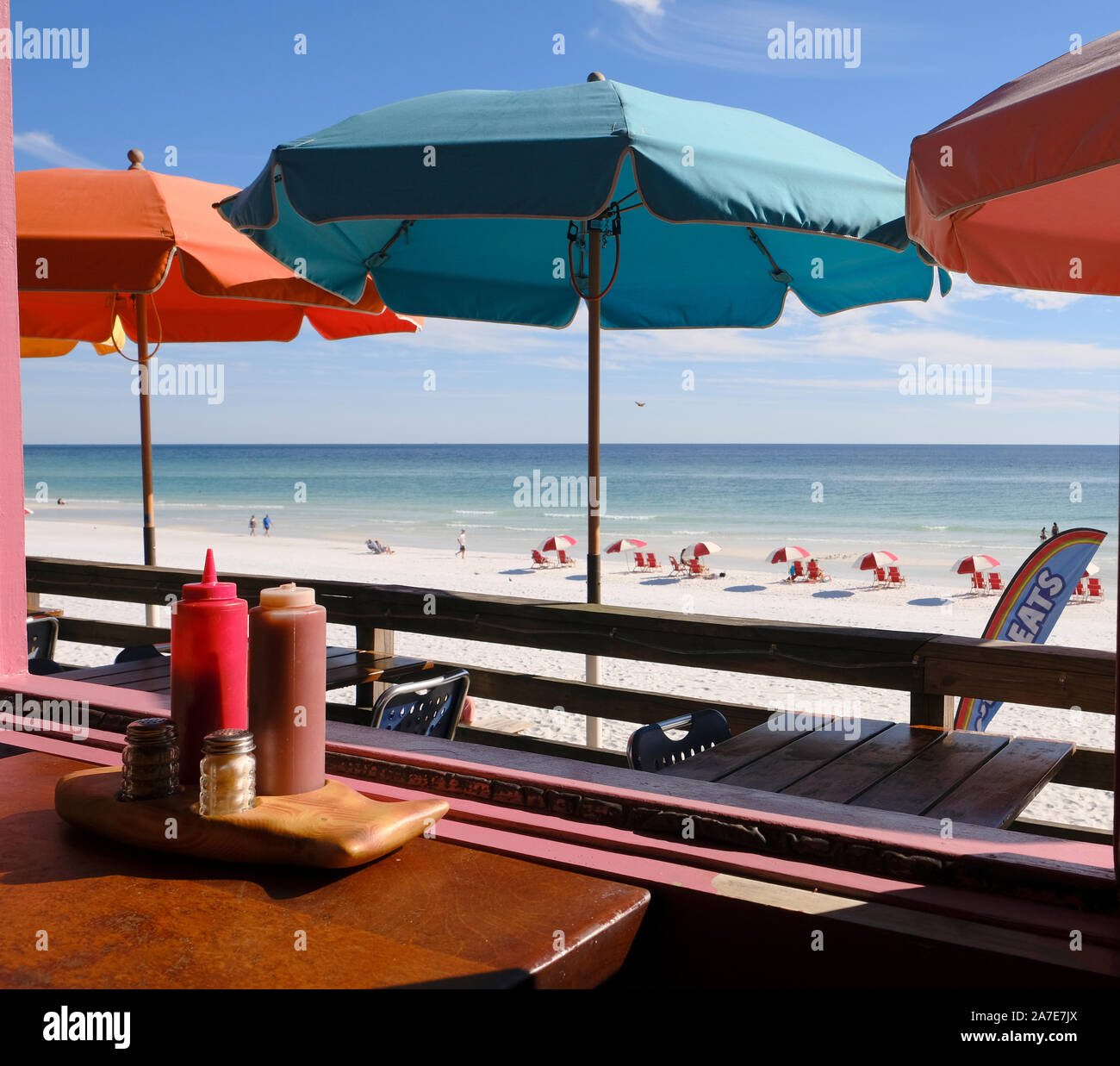 Restaurant table looking out at white sand beach and outside tables with colorful umbrellas at Pompano Joe's seafood restaurant in Miramar Beach FL. Stock Photo