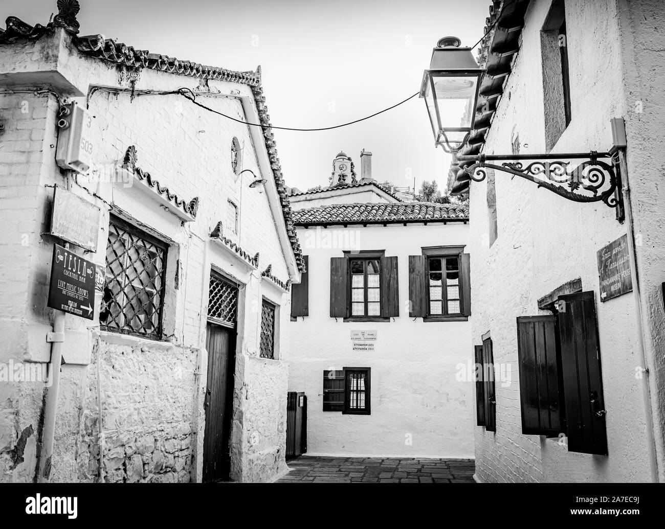 Skiathos Greece - July 31 2019; Alleyway surrounded by typically Greek Island buildings with shutters and windows and lamps with church tower in dista Stock Photo