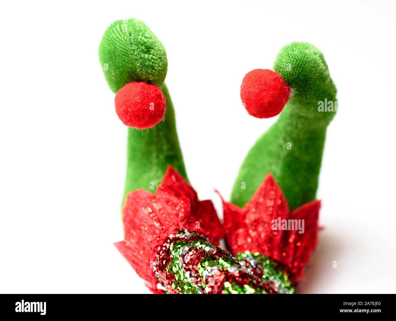 Adorable plush elf feet wearing red white and green pointy shoes with pom poms and glittered stockings with legs crossed Stock Photo