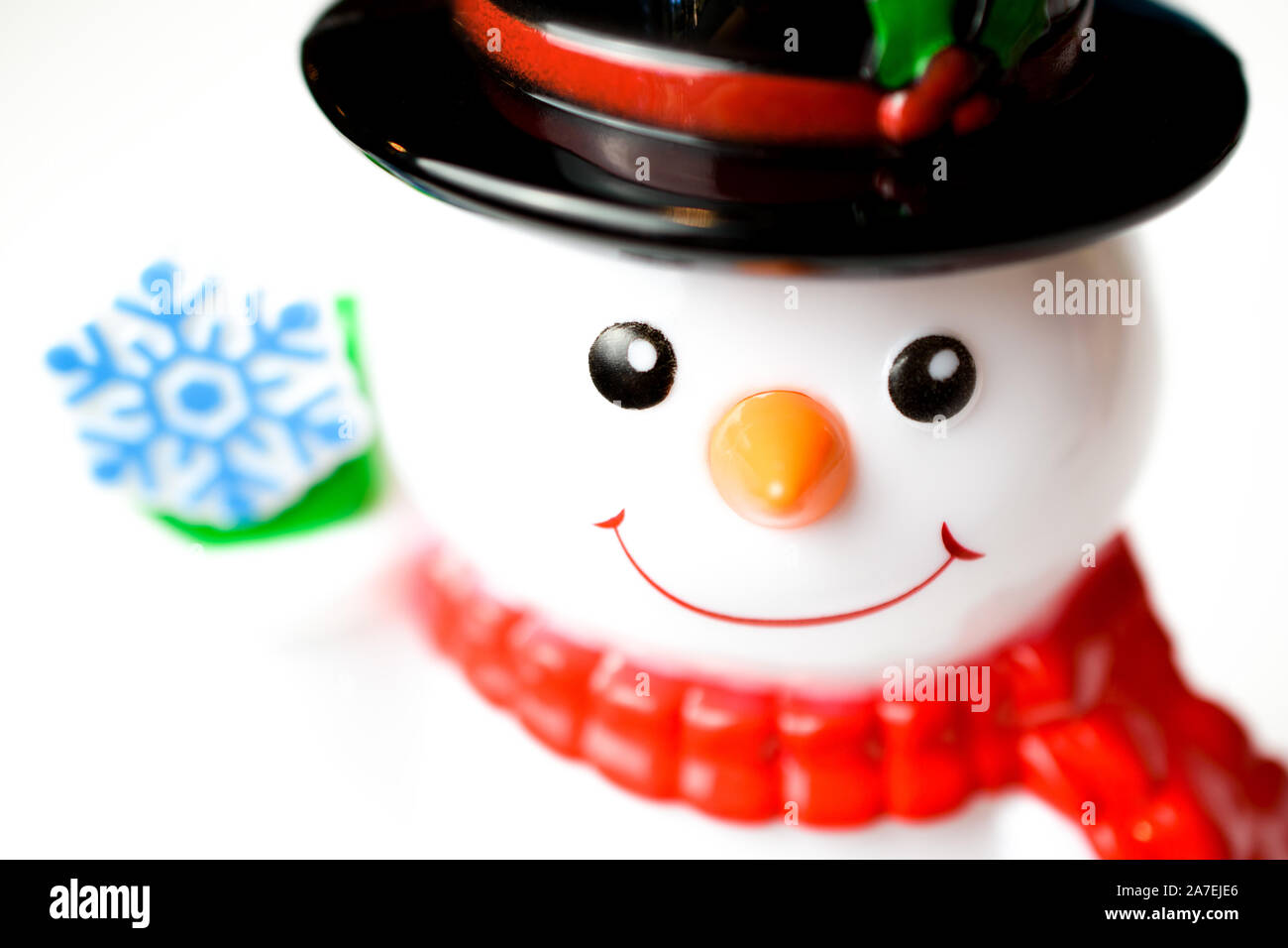 Closeup of adorable glass figurine snowman wearing a scarf and hat holding up a blue snowflake Stock Photo