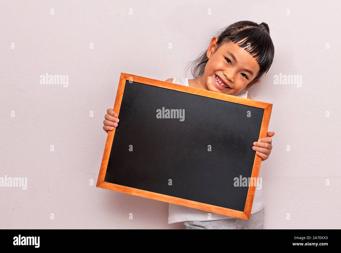 Child holding blank black board. Back to school concept. Wearing white cloth. Looking at camera. Big smile face. Stock Photo