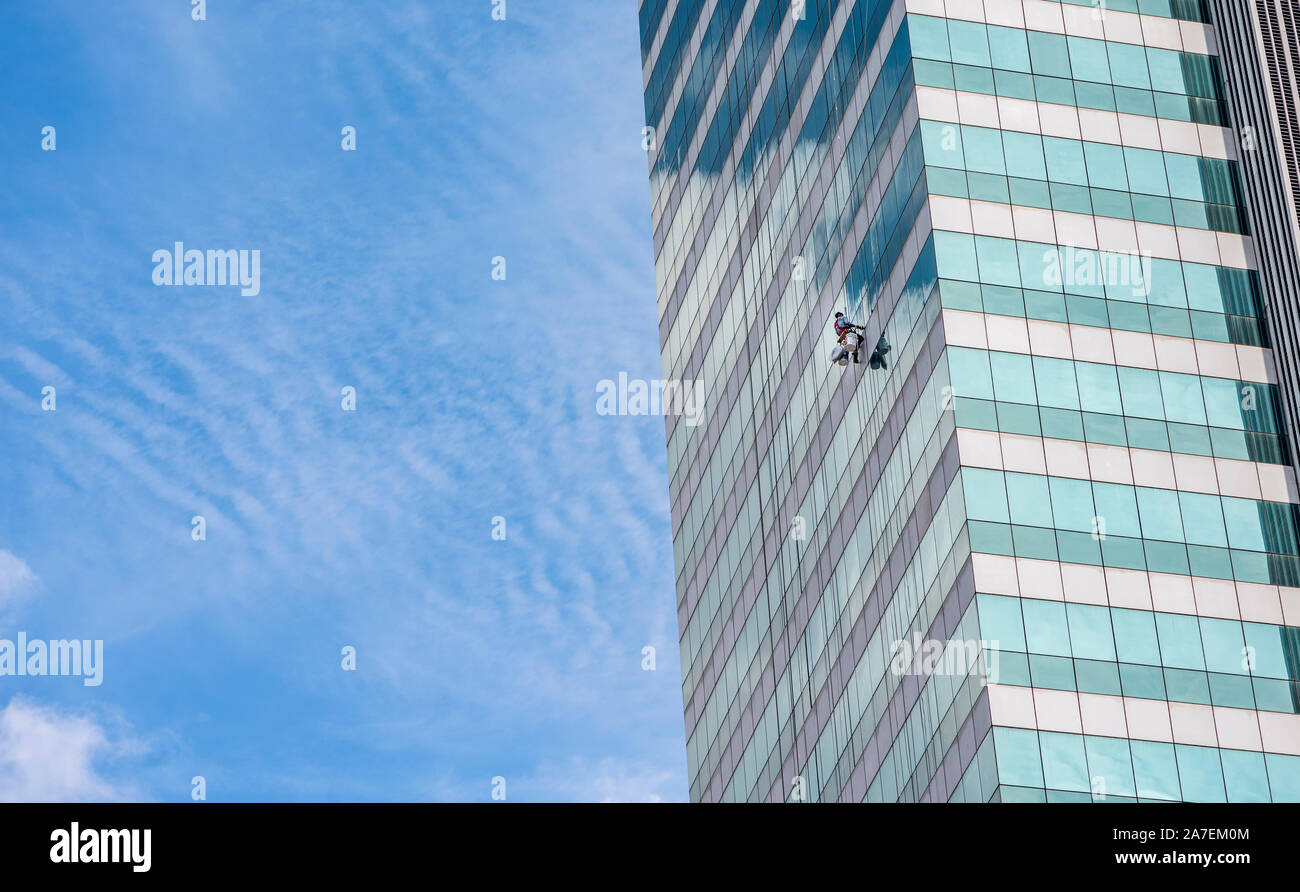 Bangkok, Thailand - Oct 14, 2017 Unidentified man cleaning window outside high office building alone in far away shot Stock Photo