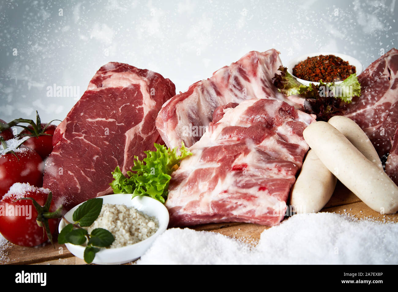 Raw beef steak, spare ribs and veal sausage on snow ready for a seasonal winter BBQ displayed with spices, and tomatoes suitable for butchery advertis Stock Photo