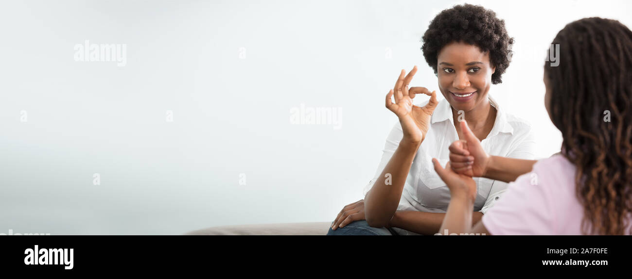 Portrait Of A Smiling African Young Woman Teaching Her Friend Hand Sign Language Stock Photo