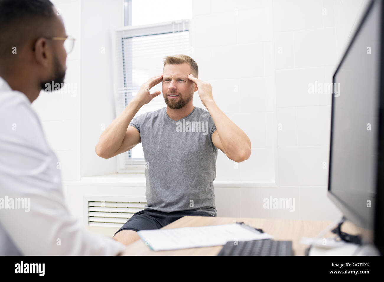 Young bearded man touching his head while complaining on permanent headache Stock Photo
