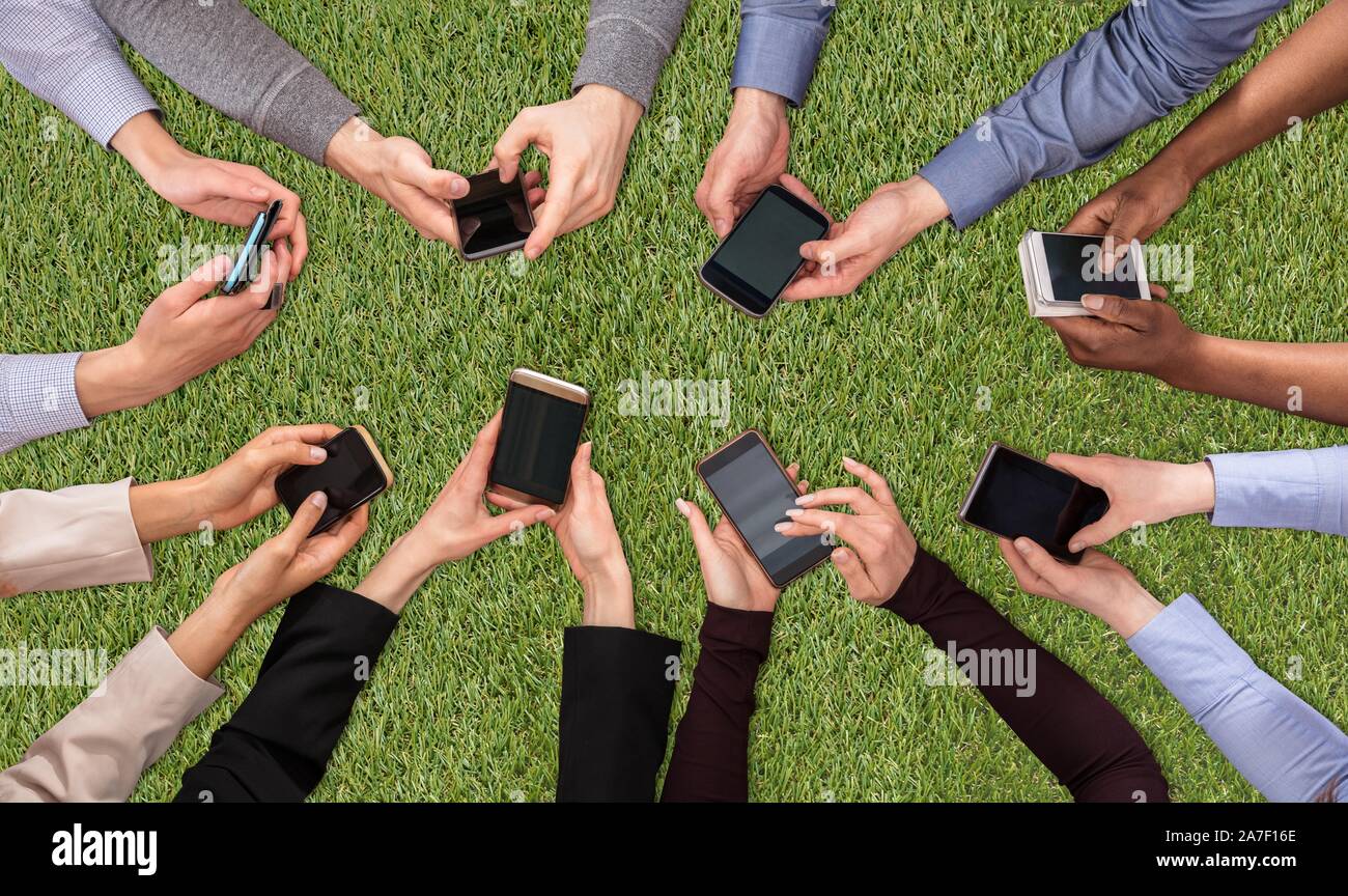 An Overhead View Of People's Hand Social Networking With Mobile Cellphones On Green Turf Background Stock Photo