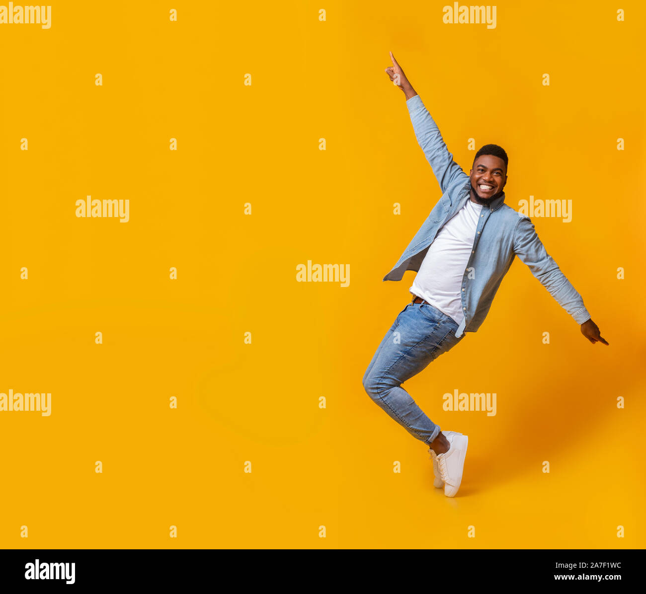 Funny black guy posing on tiptoes over yellow background in studio Stock Photo