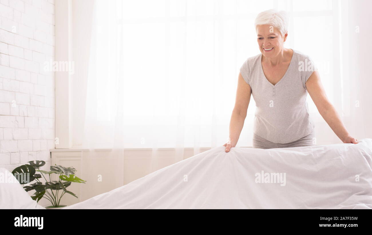 Senior woman making bed and organizing room in morning Stock Photo